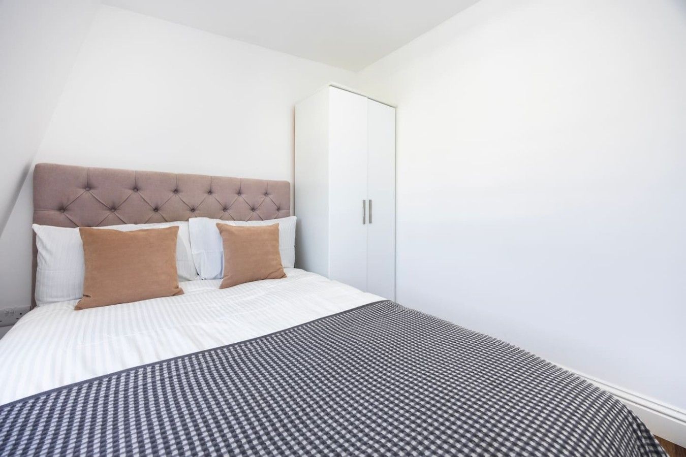 Une chambre à coucher avec une tête de lit capitonnée, un lit avec une literie blanche et marron, et une armoire dotée de poignées argentées.