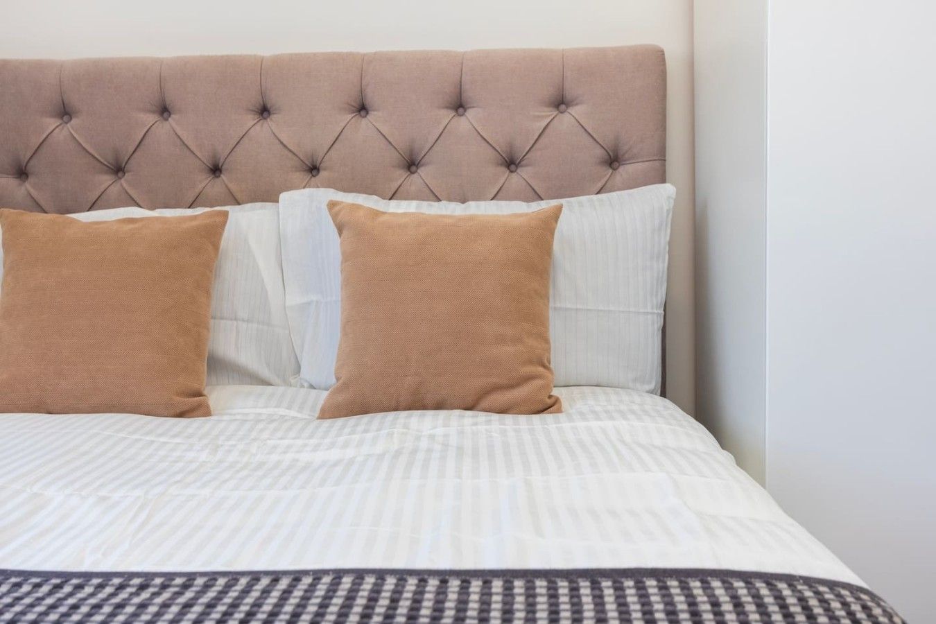 Un lit avec une tête de lit capitonnée, deux oreillers et une couvre-lit à rayures.