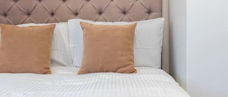 Un lit avec une tête de lit capitonnée, deux oreillers et une couvre-lit à rayures.