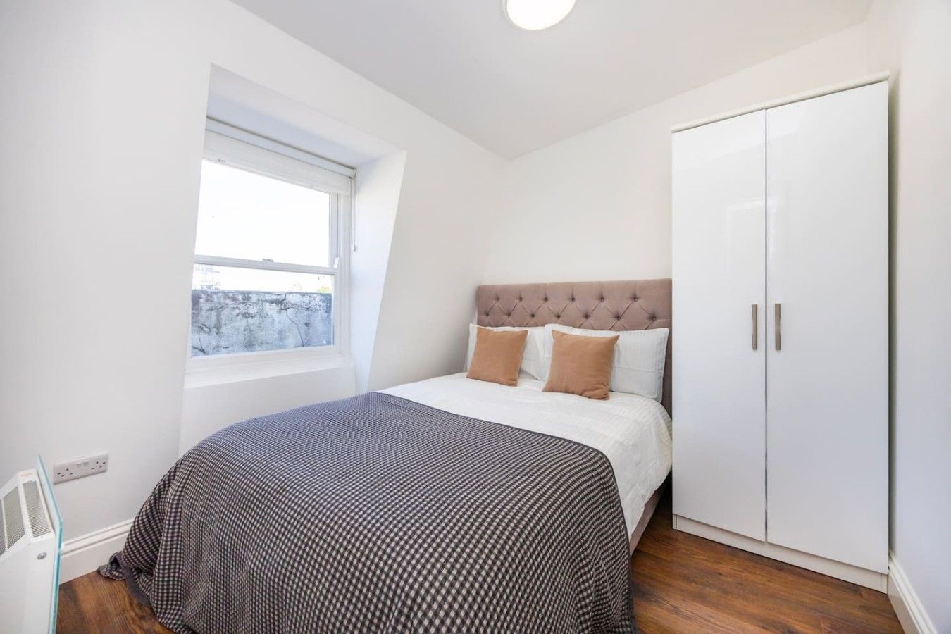 Ein Schlafzimmer mit Bett, Fenster, Kleiderschrank und Heizkörper.
