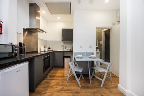 Ett kompakt kök med diskmaskin, spis och en matplats med bord och stolar.