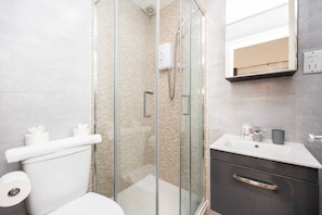 Ein modernes Badezimmer mit einer gläsernen Duschkabine, einer Toilette mit weißem Handtuch und einem Waschtisch mit Spiegel und Waschbecken.