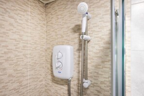 Une douche équipée d’un pommeau de douche à main et d’un panneau de commande fixé au mur.