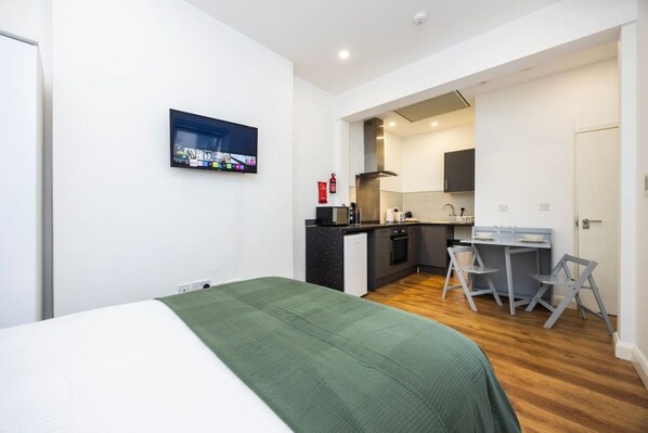 Ein kleines Hotelzimmer mit Bett, einer Kochnische und einem Essbereich mit Stühlen.