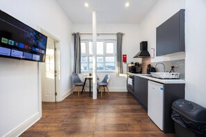A compact kitchen with a dining area, a TV mounted on the wall, and a window with curtains. - Earl`s Court Residence | Elegant 1BR | London (Greater London)