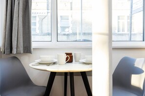 Una habitación con una mesa puesta para dos, una ventana con cortinas y vistas a edificios.