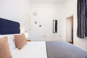 Una habitación de hotel con una cama, una mesita de noche, una lámpara, un espejo y una puerta que da a otra habitación.