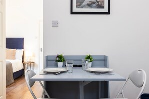 A compact dining area with a table set for two, two small potted plants, and a framed picture on the wall. - Earl`s Court Residence | Stylish 1BR | London (Greater London)