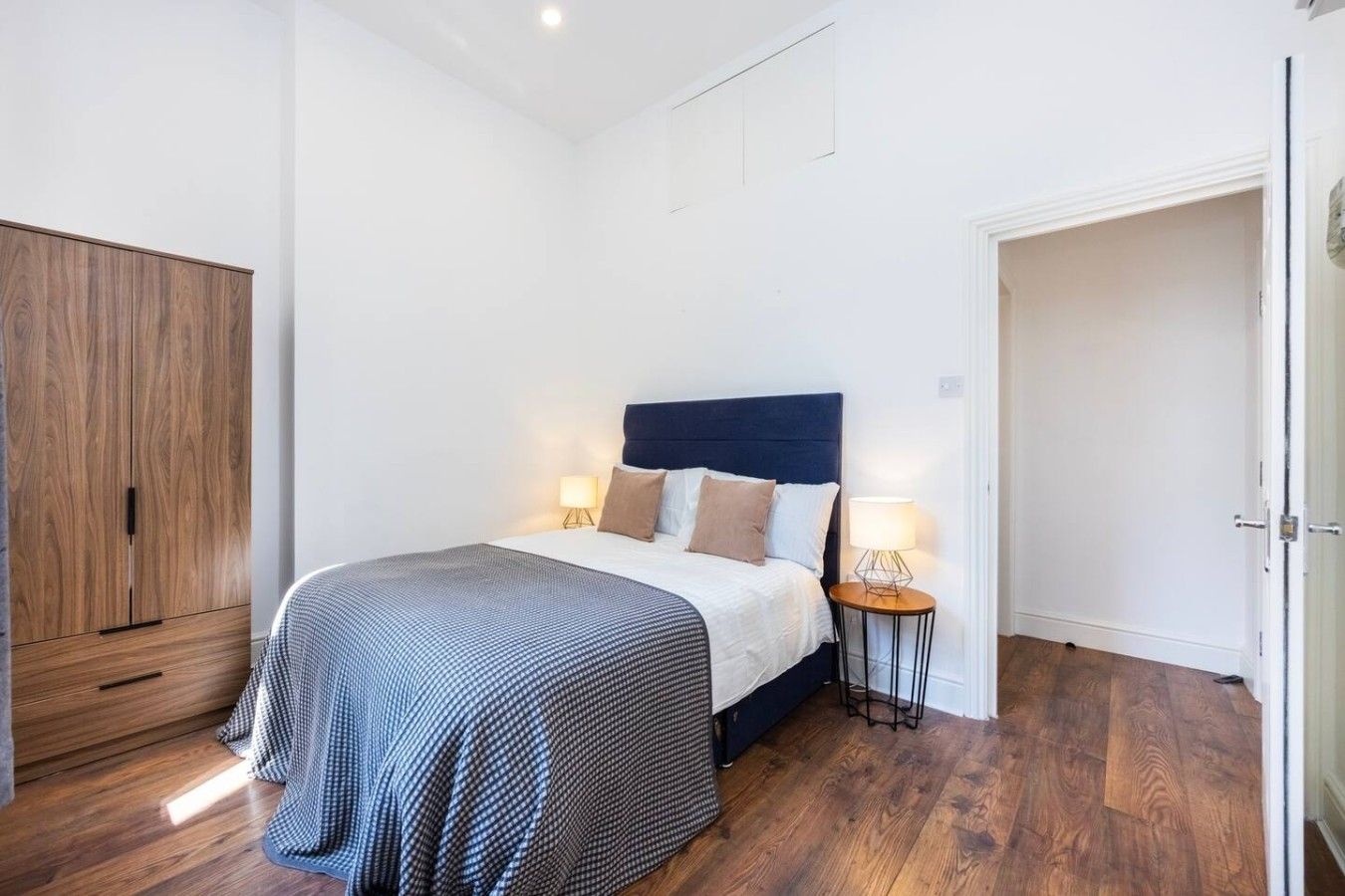 Un dormitorio con cama, mesitas de noche, armario y puerta.