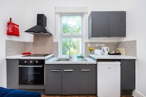 A compact kitchen with a stove, oven, sink, and a small refrigerator. - Earl`s Court Residence | Stylish 1BR | London (Greater London)