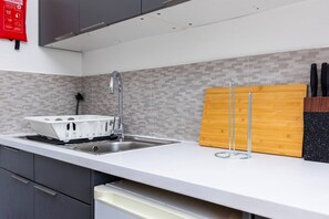 A modern kitchen with a white countertop, stainless steel sink, and a wooden cutting board. - Earl`s Court Residence | Elegant 2BR | London (Greater London)