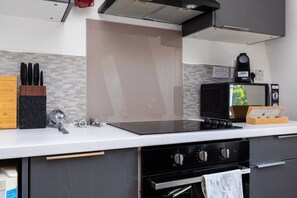 A modern kitchen with a black stove, a microwave, and a coffee machine. - Earl`s Court Residence | Elegant 2BR | London (Greater London)