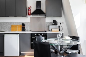 A modern kitchen with a glass dining table, black chairs, a built-in oven, a coffee maker, and a fire extinguisher. - Earl`s Court Residence | Elegant 2BR | London (Greater London)