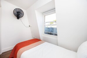 A bedroom with a single bed, a window with a view, and a wall-mounted fan. - Earl`s Court Residence | Elegant 2BR | London (Greater London)