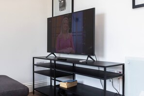 A flat-screen TV on a black TV stand with a shelf below. - Earl`s Court Residence | Elegant 2BR | London (Greater London)