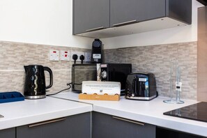 A modern kitchen with a coffee maker, toaster, and kettle on the counter, and a sign indicating the availability of Nespresso beverages. - Earl`s Court Residence | Elegant Studio | London (Greater London)