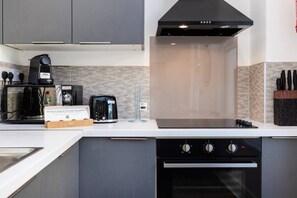 A modern kitchen with grey cabinets, a coffee maker, a toaster, and a built-in oven. - Earl`s Court Residence | Elegant Studio | London (Greater London)