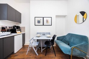A compact kitchen with modern appliances, a dining table with chairs, and a blue sofa. - Earl`s Court Residence | Elegant 1BR | London (Greater London)