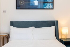 A hotel room with a bed, a nightstand, a lamp, and a framed artwork on the wall. - Earl`s Court Residence | Elegant 1BR | London (Greater London)