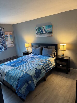 A bedroom with a bed, two bedside tables, a nightstand, a painting, and a curtain.