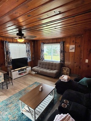 A cozy living room with a sofa, a coffee table, a TV, and a fan.