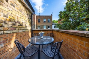 A brick wall with a glass table and four chairs, a small vase with flowers, and a view of a brick building across the street. - Earl`s Court Residence | Stylish Studio | London (Greater London)