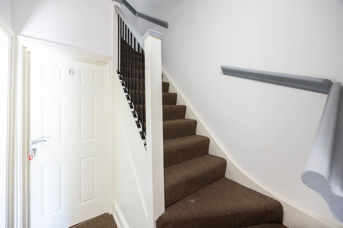 A staircase with a handrail, a white door with a number, and a carpeted floor.