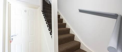 A staircase with a handrail, a white door with a number, and a carpeted floor.