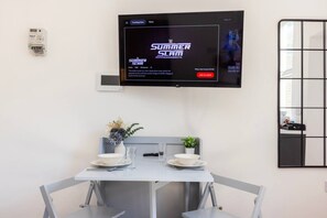 A modern dining area with a TV displaying 'Summer Slam Minnesota' on the wall, a table set with plates and glasses, and a small plant on the table. - Earl`s Court Residence | Stylish Studio | London (Greater London)