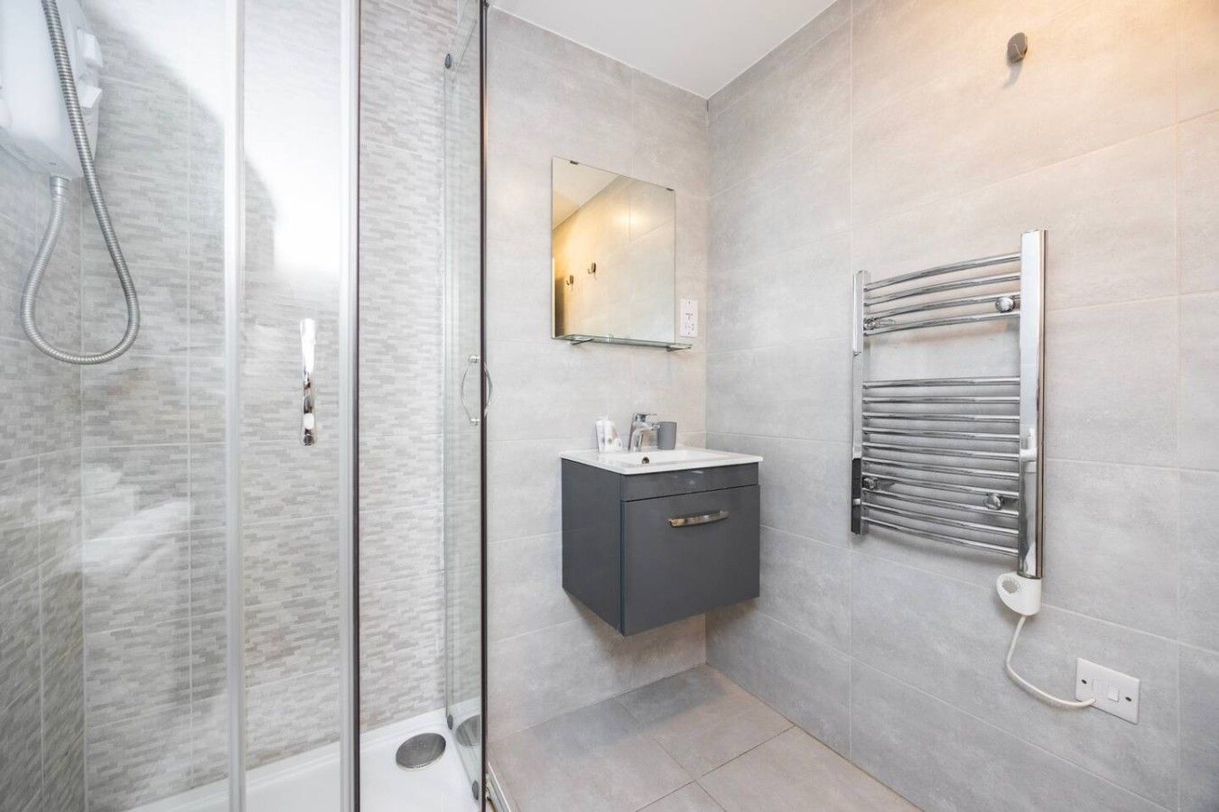 A modern bathroom with a glass shower enclosure, a vanity with a mirror, and a built-in towel rack.