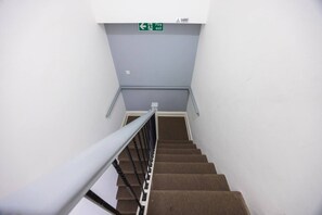 Una scala con un cartello di uscita di sicurezza sopra, un corrimano sul lato sinistro e una parete blu.