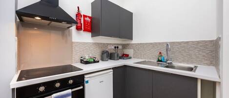 A compact kitchen with a stove, oven, and dishwasher, a sink with a modern faucet, and a microwave.