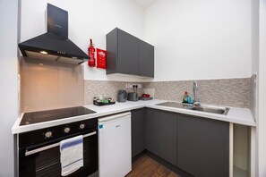 Una cucina compatta con piano cottura, forno e lavastoviglie, un lavello dotato di un rubinetto moderno e un forno a microonde.
