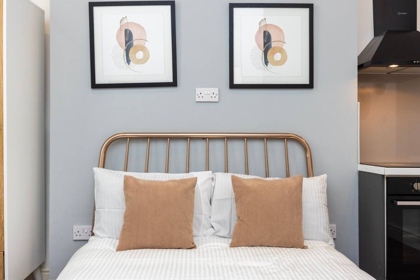 Una cama con cabecera de metal, dos almohadas y dos obras de arte abstractas enmarcadas en la pared.