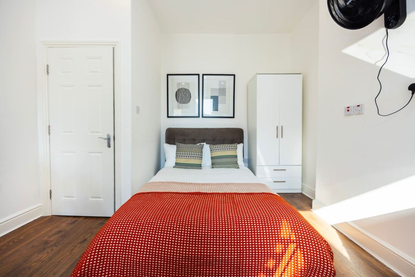 Ein Schlafzimmer mit Bett, Kleiderschrank und Wandventilator.