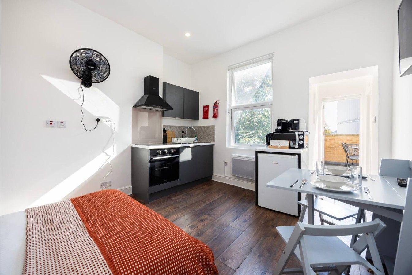 A compact kitchen with a stove, microwave, and sink, a dining area with a table and chairs, and a window providing natural light.