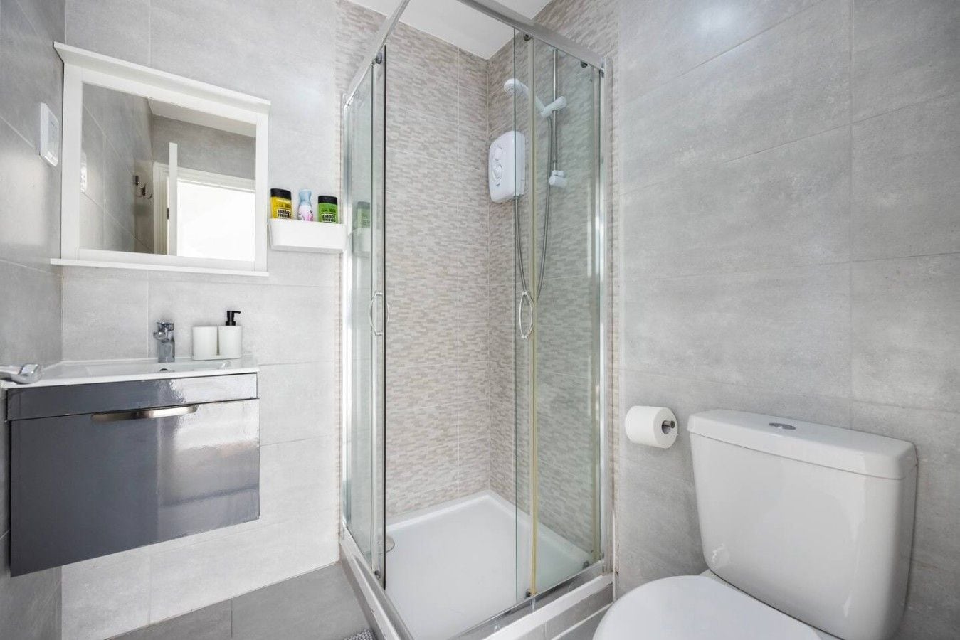 A modern bathroom with a glass-enclosed shower, a white toilet, and a stainless steel sink.