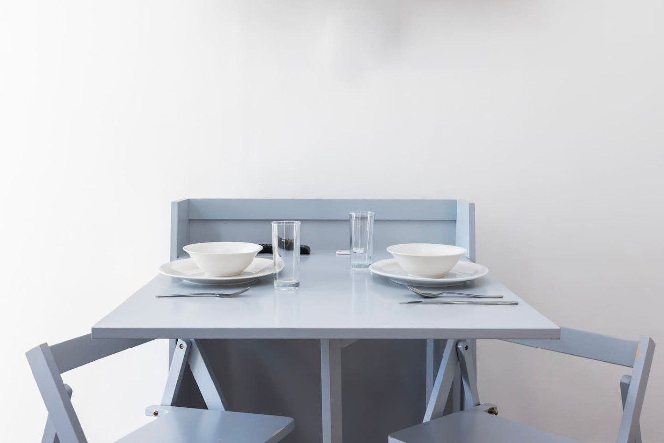 Une table à manger au design minimaliste, agrémentée de deux bols blancs, deux assiettes et deux verres.