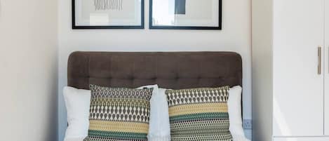 A neatly made bed with patterned pillows, a tufted headboard, and a white wardrobe with gold handles.