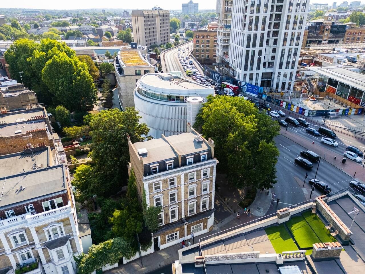 An urban street scene with a mix of modern and traditional architecture, including a curved building with a glass facade and a classic building with a white facade.
