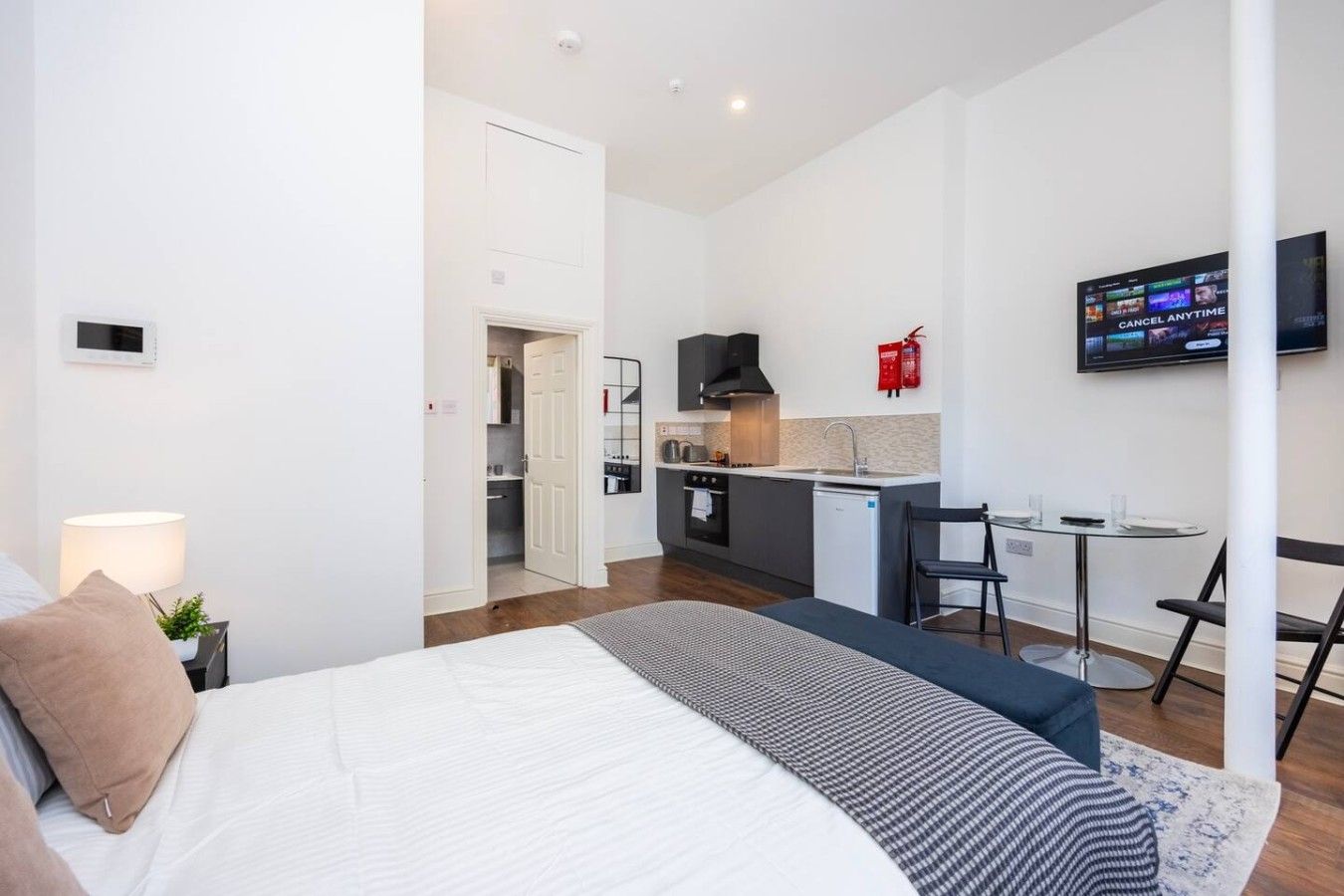 Ein modernes Hotelzimmer mit Bett, Schreibtisch, Küchenzeile und Fernseher.