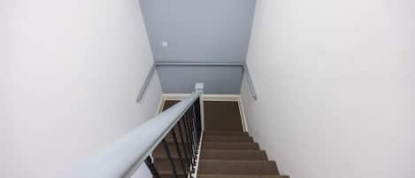 A staircase with a fire exit sign above, a metal handrail, and carpeted steps.