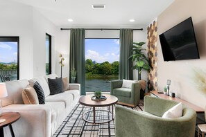 A modern living room with a sofa, armchairs, a coffee table, and a TV mounted on the wall. - Riverview Luxury Condo with Garage, Balcony, Downtown (Nashville)