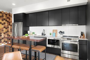 A modern kitchen with black cabinets, stainless steel appliances, a wooden dining table, and a hexagonal tile backsplash. - Riverview Luxury Condo with Garage, Balcony, Downtown (Nashville)