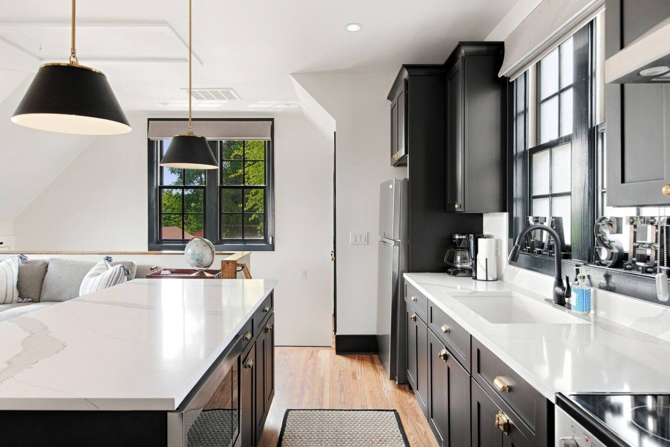 A modern kitchen with a central island, dark cabinetry, and a large window providing natural light.