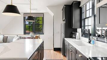 A modern kitchen with a central island, dark cabinetry, and a large window providing natural light.