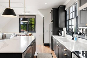 A modern kitchen with a central island, dark cabinetry, and a large window providing natural light. - Only 2 miles Downtown, Walk to 5 Points + Free Parking (Nashville)