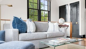 A modern living room with a grey sofa, a glass coffee table, and a large window with a view of trees.