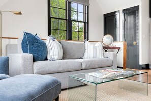 Una sala moderna con un sofá gris, una mesa de centro de vidrio y un ventanal con vistas a árboles.