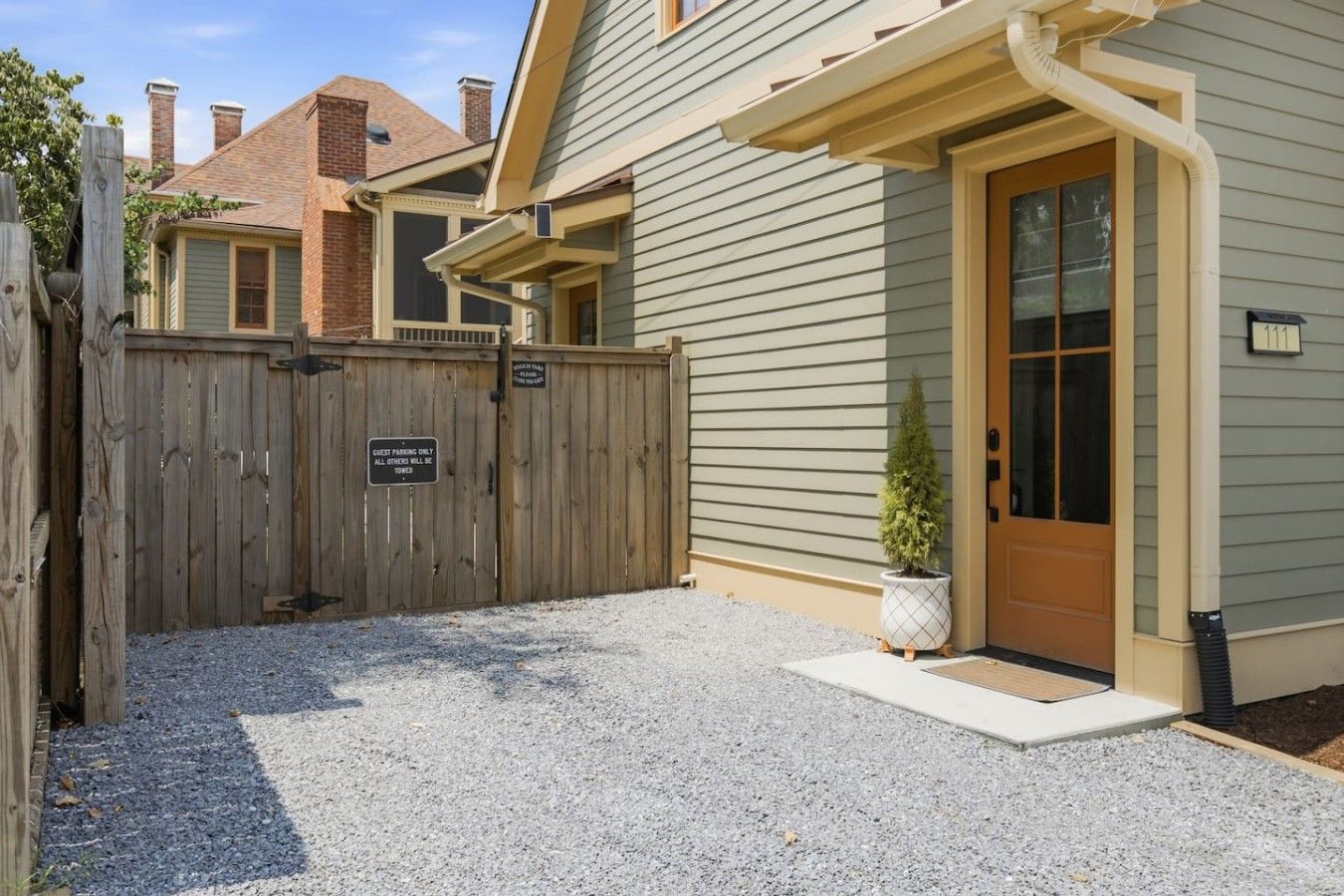 A gated entrance to a building with a wooden fence, a gravel driveway, and a potted plant near the door.